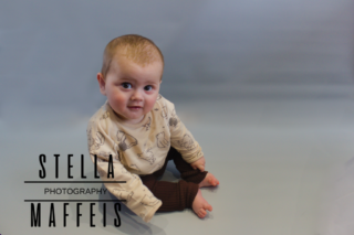 A smiling big eyed baby sitting up in a whinnie the poo shirt.