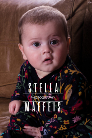 Big eyed baby looking curiously at the camera, sitting on a couch.