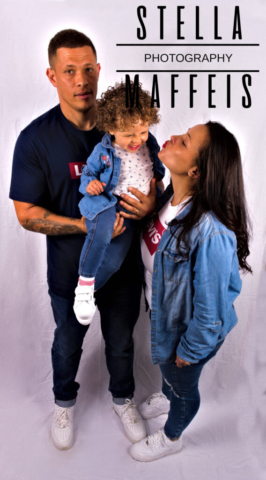 A curly, smiling toddler being held by her dad while her mommy tries to kiss her cheek.