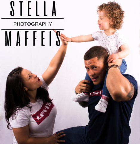 Mother giving her toddler a high five, who is sitting on her dads shoulders.