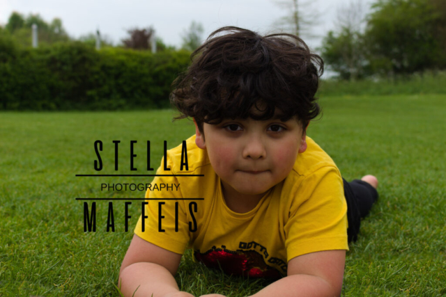 A little boy lying on the grass outside.