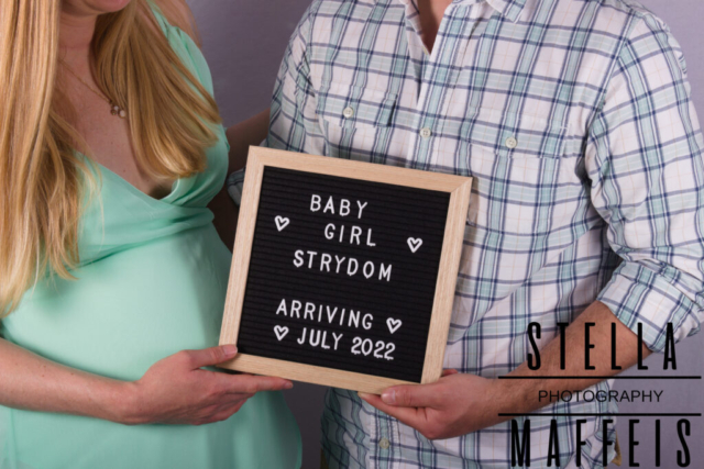 Expecting mother and father holding a sign which reads "Baby Girl Strydom Arriving July 2022".