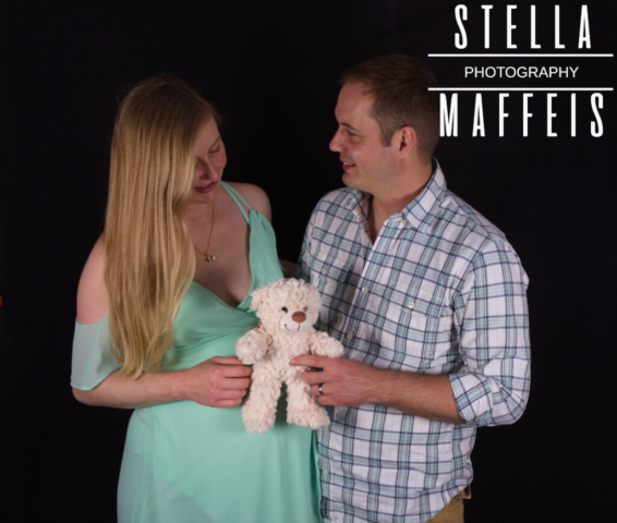 Happy pregnant couple smiling at each other while holding a white teddy.