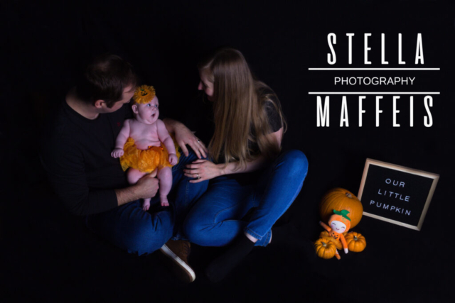 Baby in an orange tutu sitting on the floor with her parents, pumpkin decorations nearby and a sign that reads "Our Little Pumpkin".