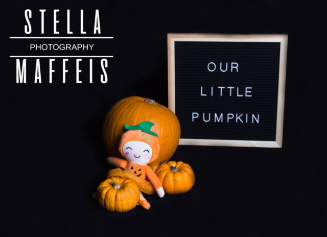 Three pumpkins, a little pumpkin dressed doll and a sign that reads "Our Little Pumpkin".
